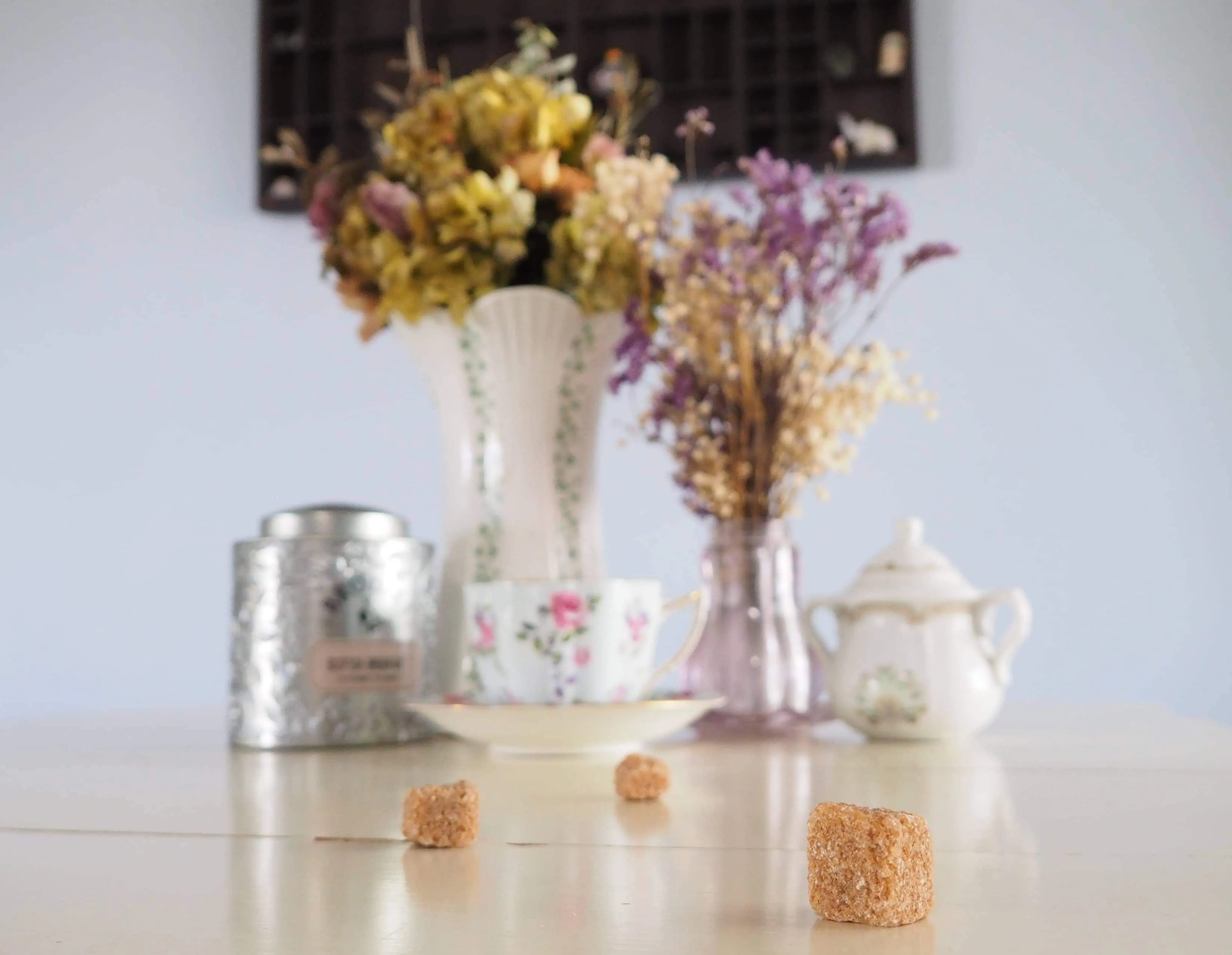 Brown sugar cubes in front of a tea setting and flowers.