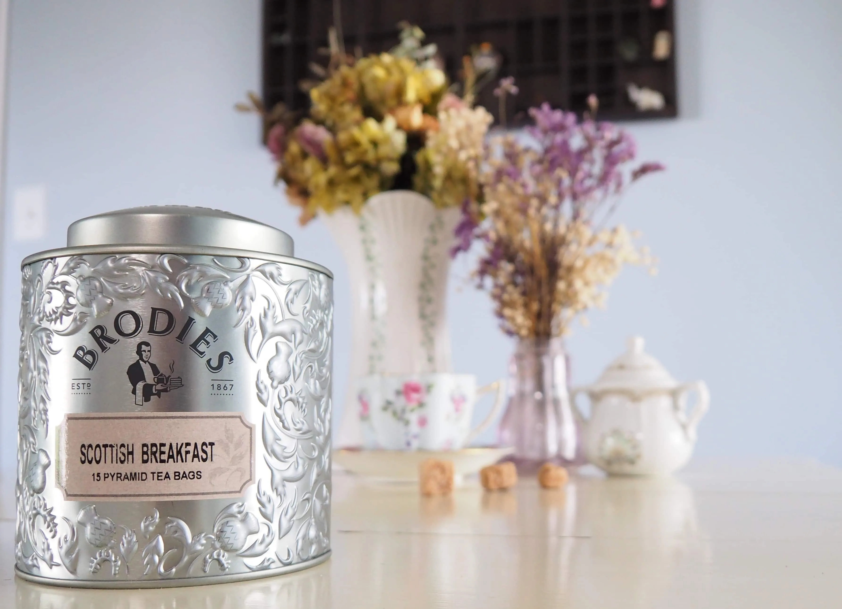Brodies tea tin in front of tea setting and flowers.